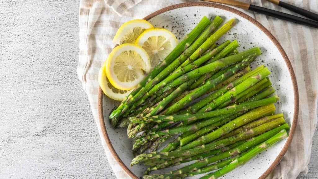 Asparagus on a plate with lemon wedges.