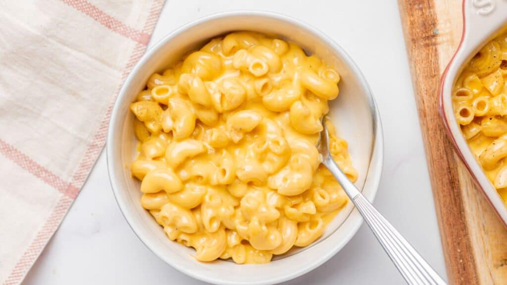 Two bowls of macaroni and cheese on a wooden cutting board.