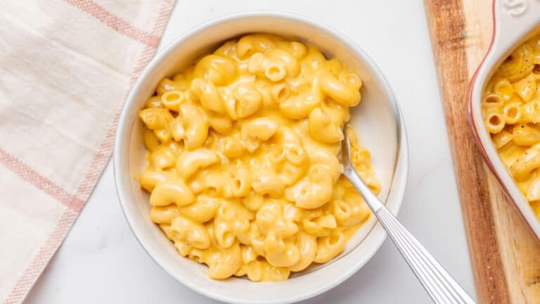 Two bowls of macaroni and cheese on a wooden cutting board.