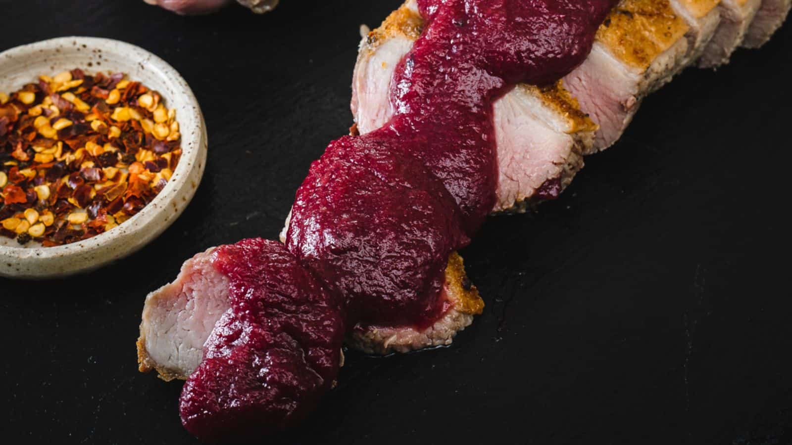 Pork with cranberry sauce on a black background.