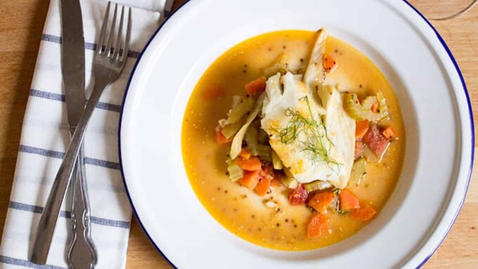 A white plate with a bowl of soup and a glass of wine.