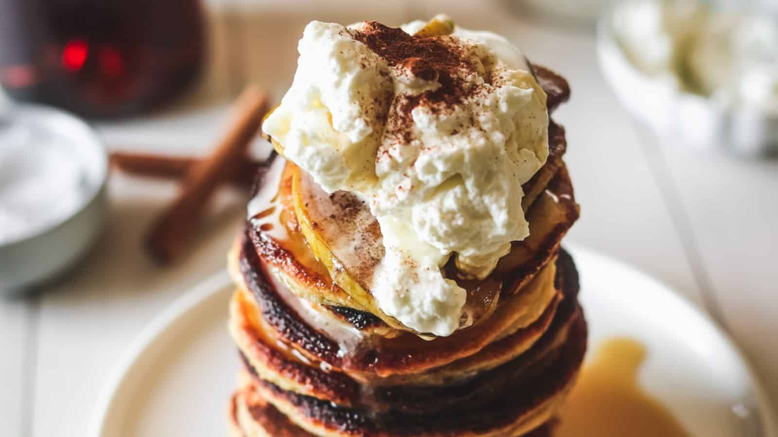 A stack of pancakes topped with whipped cream and cinnamon.