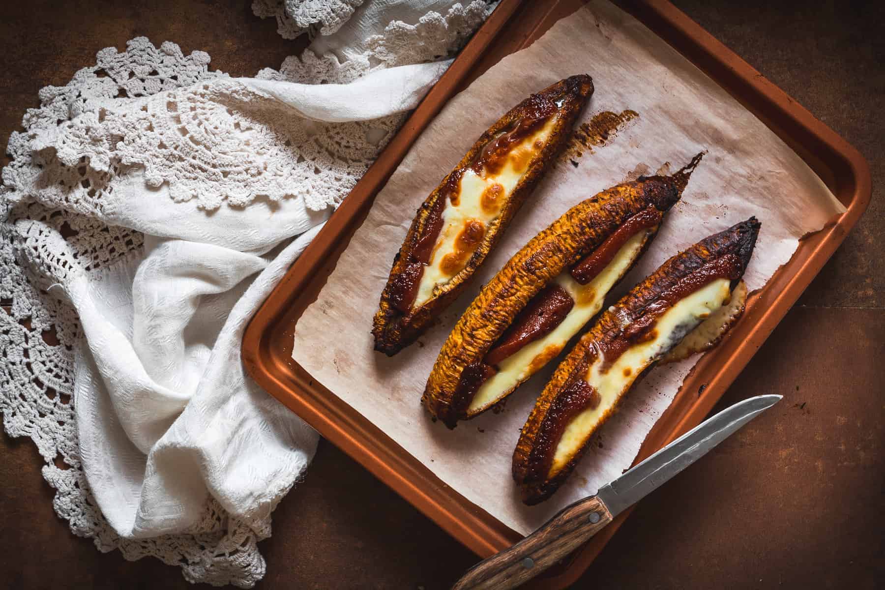 Three grilled bananas on a baking sheet with a knife.