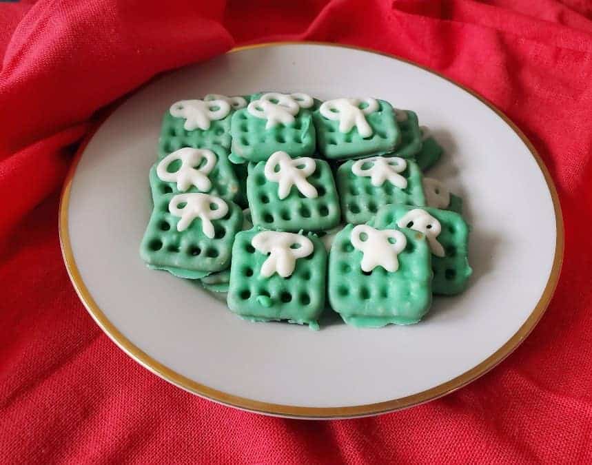 Chocolate covered Christmas pretzels sit in a pile on a white plate.