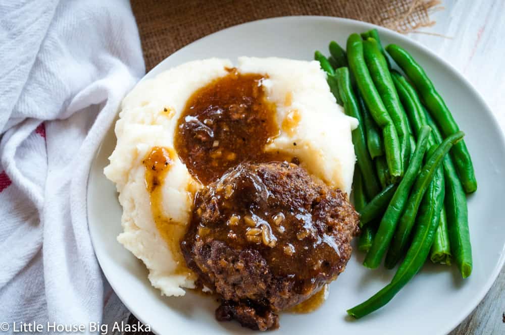 Salisbury steak on a plate with green beans and mashed potatoes.