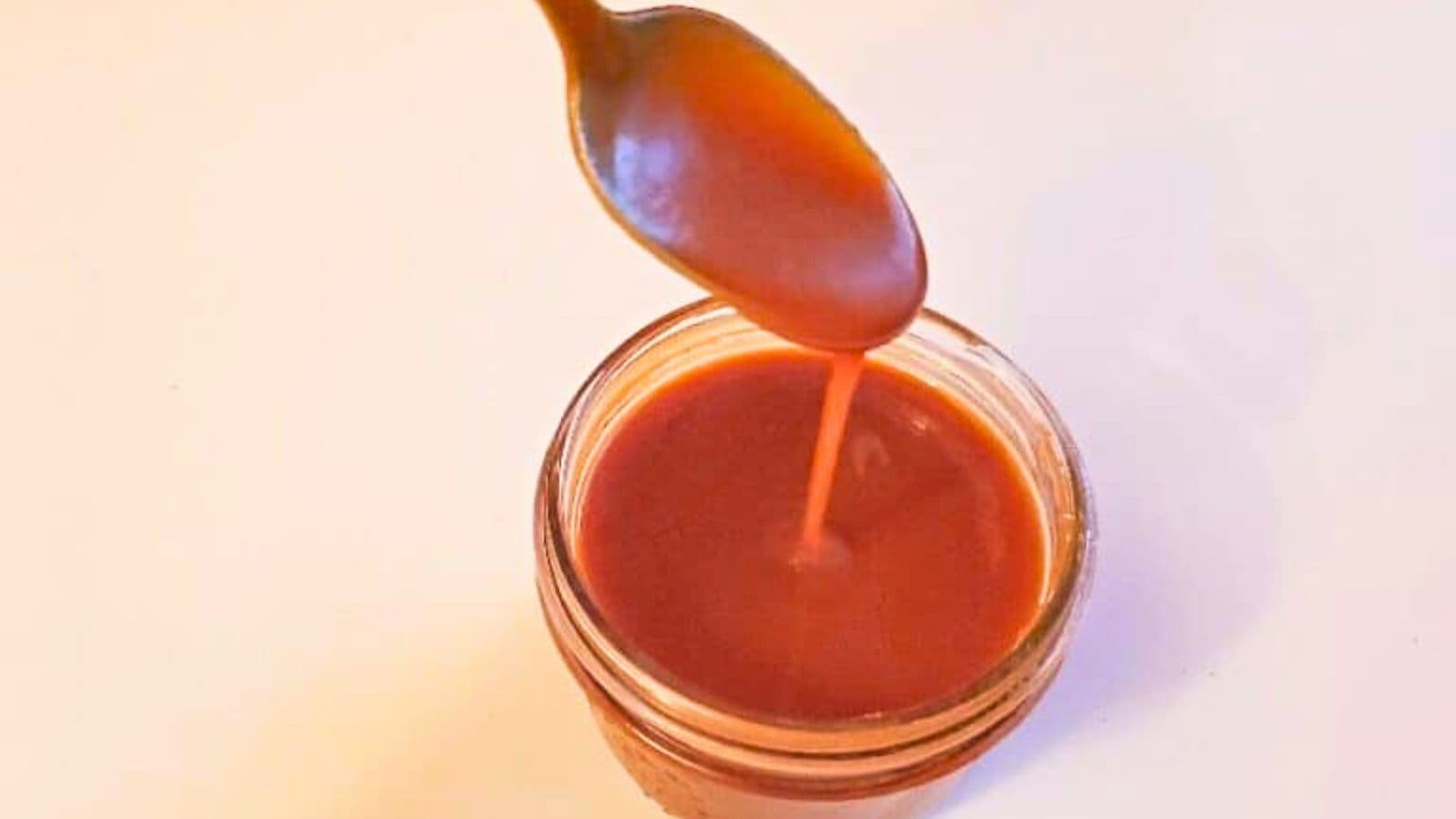 Image shows a spoon drizzling caramel sauce back into its jar.