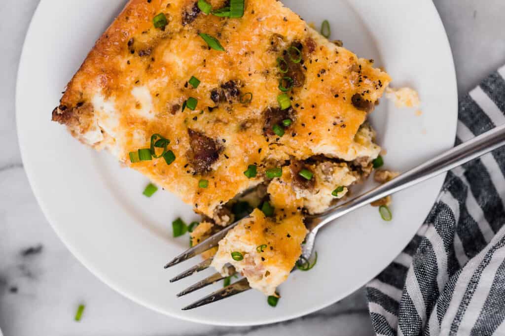 A slice of breakfast casserole on a plate with a fork.