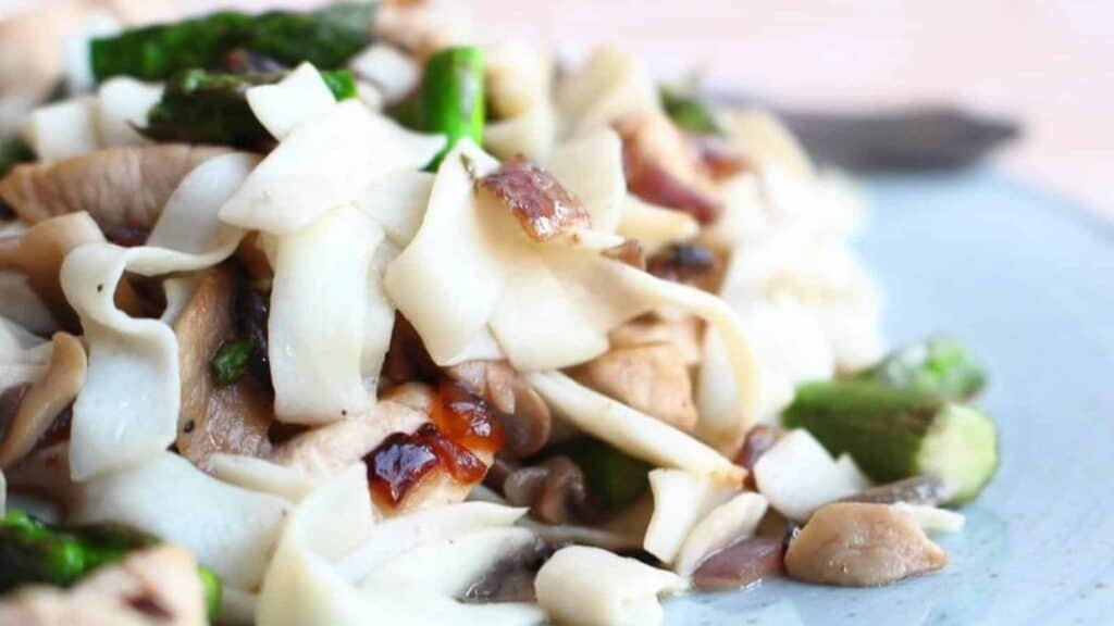 A plate with noodles, mushrooms and asparagus.