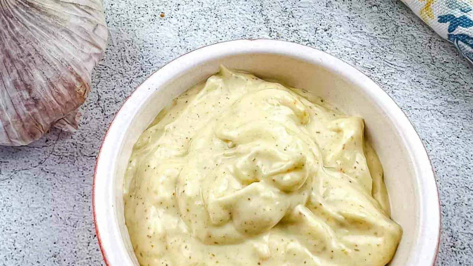 A bowl of garlic aioli dip with a clove of garlic next to it.