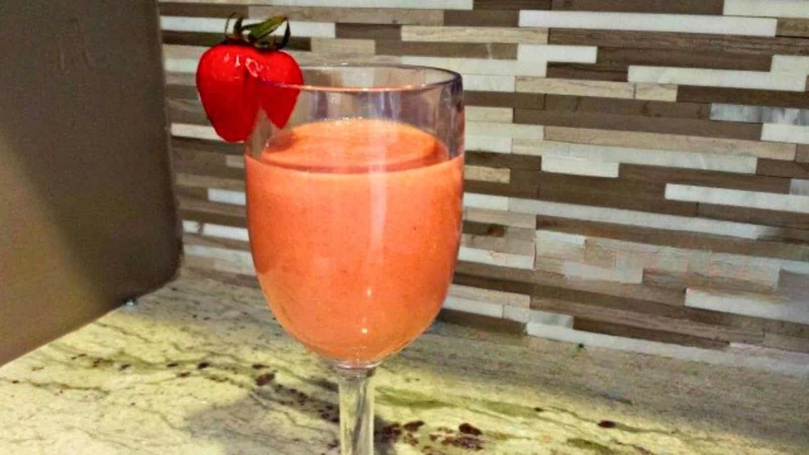 Image shows a strawberry lemonade cocktail  with a strawberry on the side of the glass.