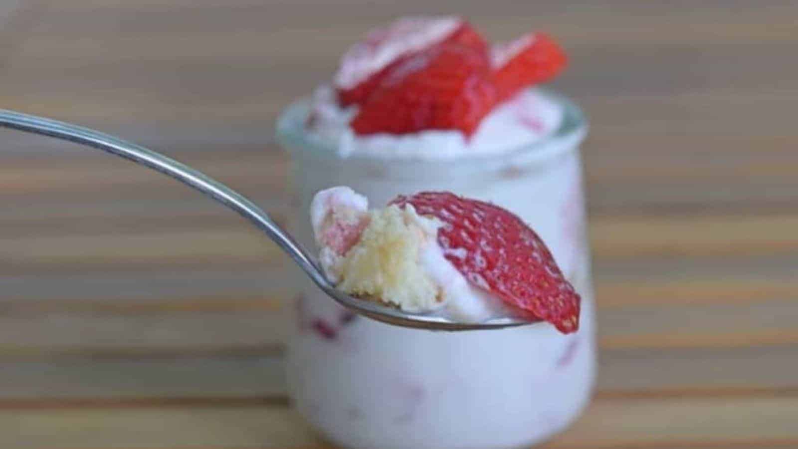 Image shows a spoon holding a scoop of the strawberry lemonade icebox cake with a small jar of the dessert behind it.