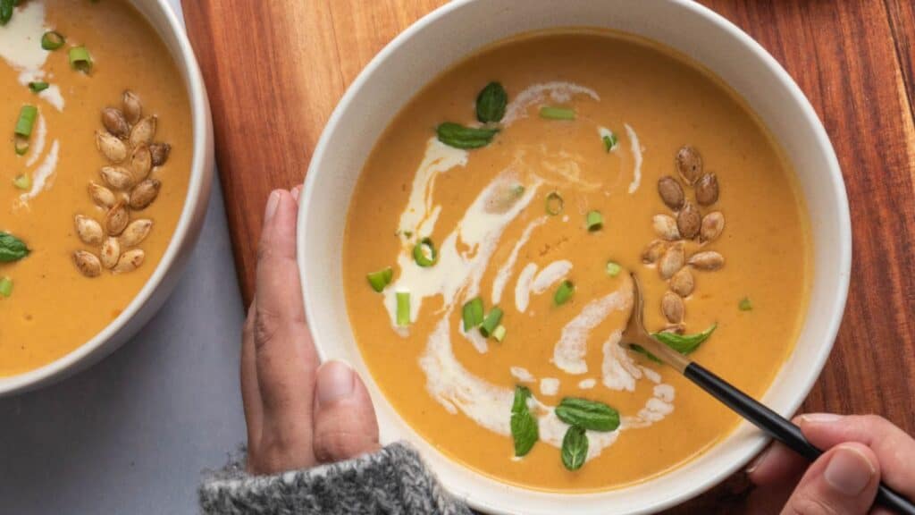 Two bowls of butternut squash soup on a wooden table.