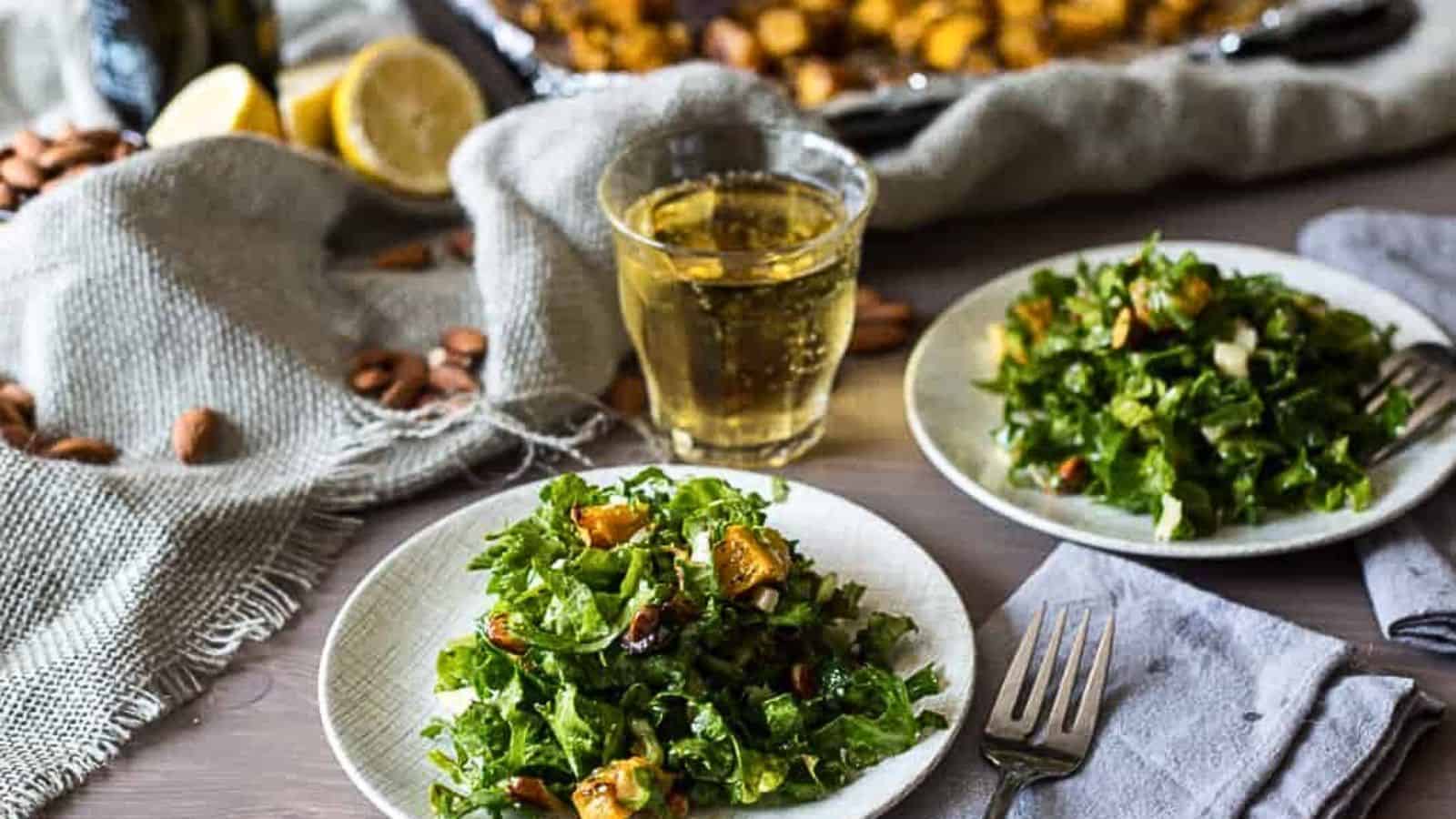 A plate of kale salad on a table next to a glass of wine.