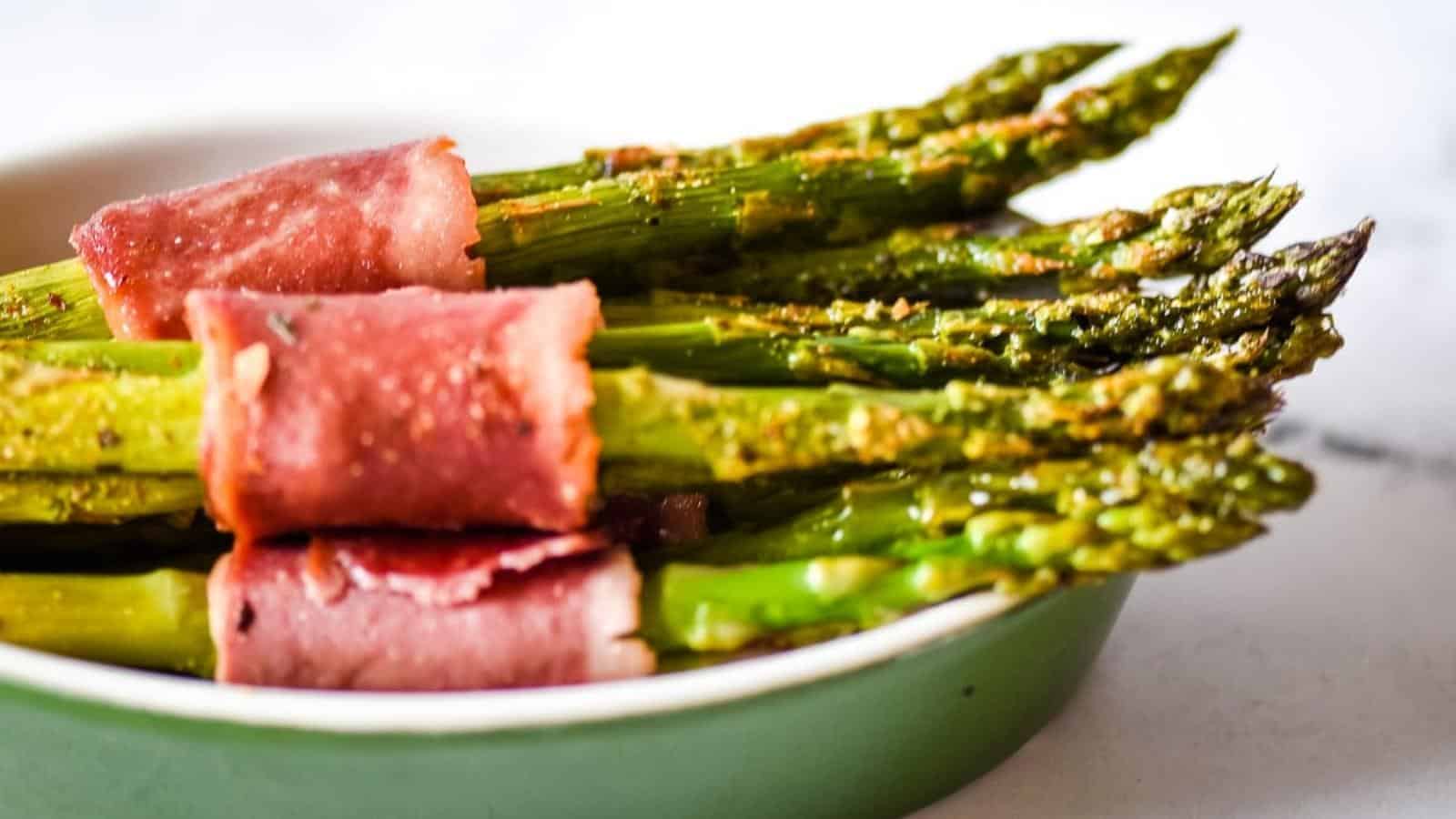 Asparagus wrapped in bacon in a green bowl.