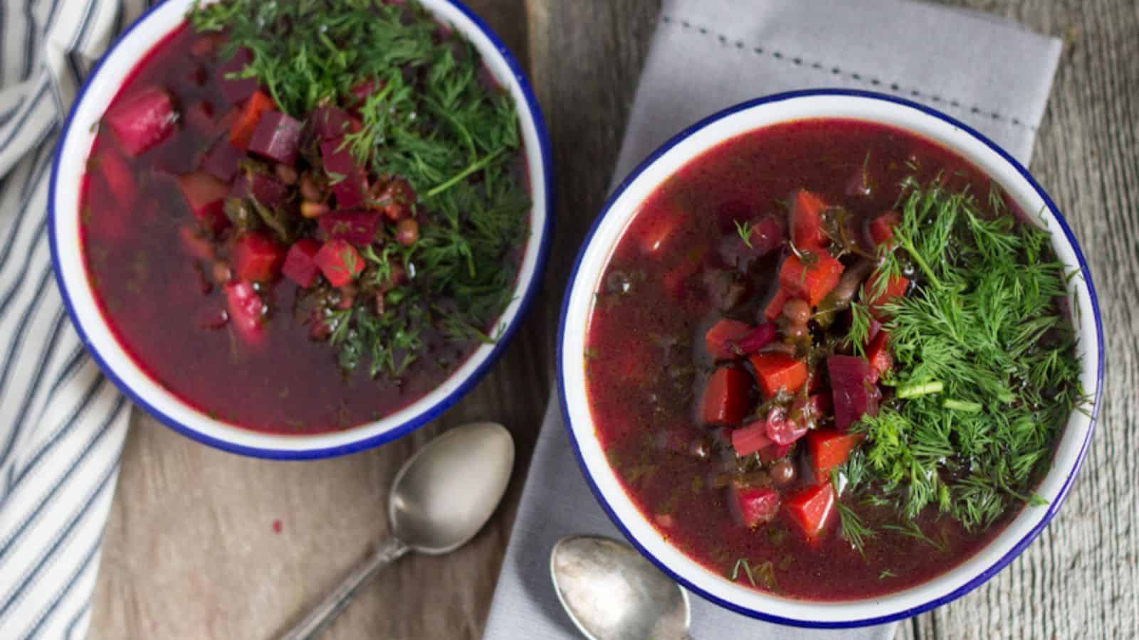 Two bowls of beetroot soup on a wooden table.