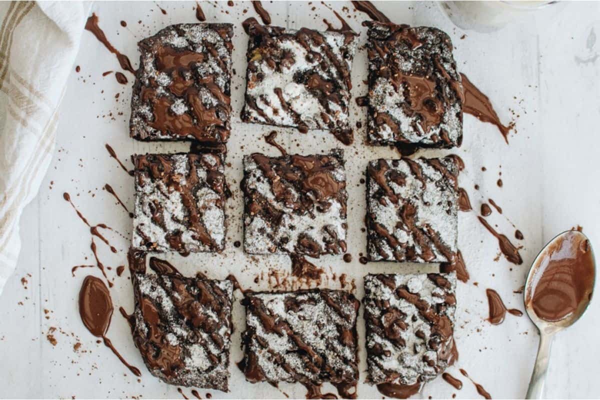 A plate of chocolate brownies with icing and a spoon.