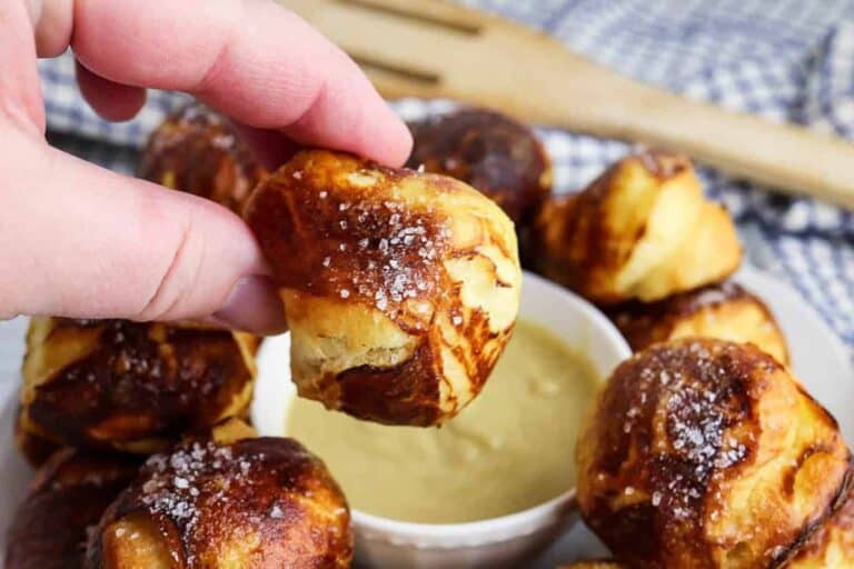 A person dipping a pretzel into a dipping sauce.