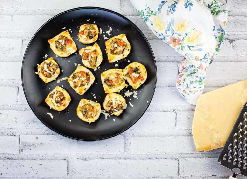 A black plate with bacon and mushroom tartlets on it.