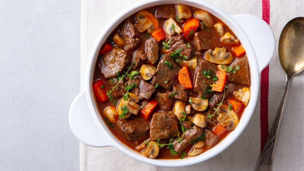 Beef stew with mushrooms and carrots in a white bowl.