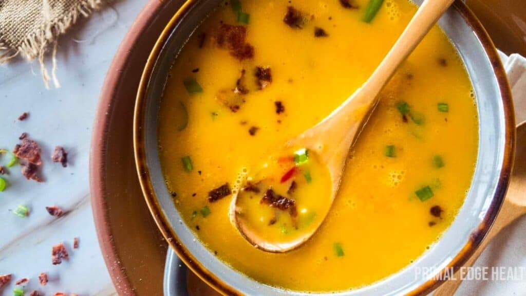 A wooden spoon in a bowl of beer cheese soup with bacon and green onion garnish.