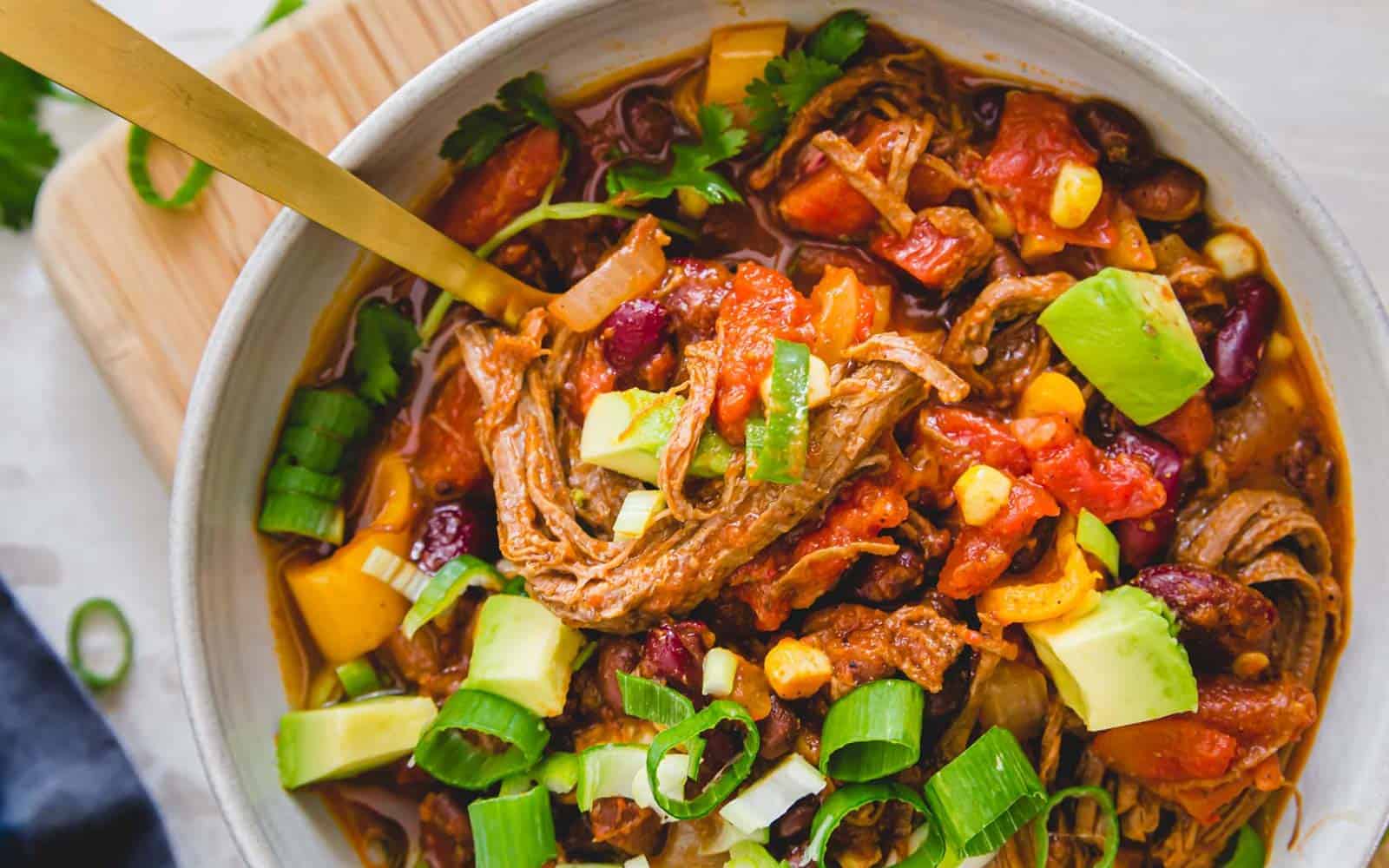 Brisket chili in a bowl topede with green onions and avocado.