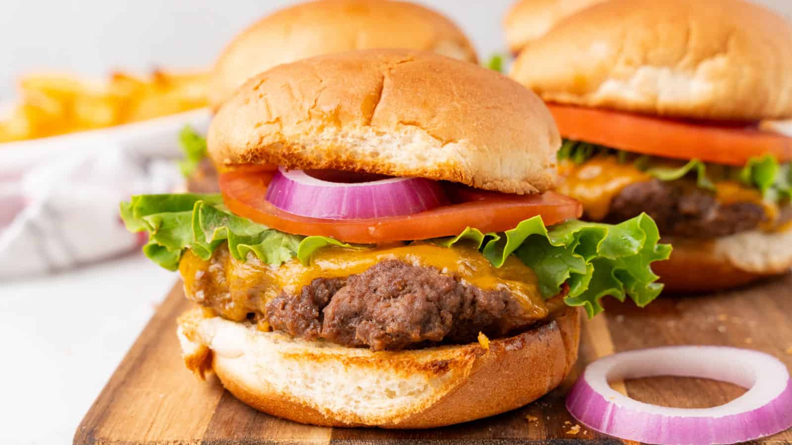 A cheeseburger on a bun with lettuce, tomato, onion on a wood board.