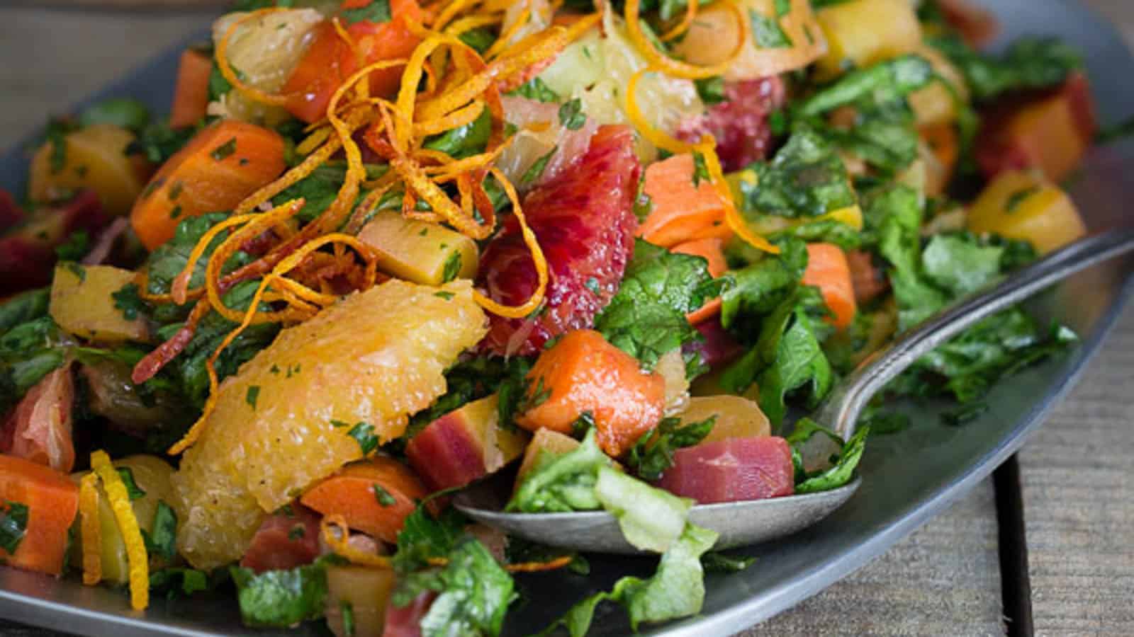 Carrot citrus salad on a metal platter with spoon.