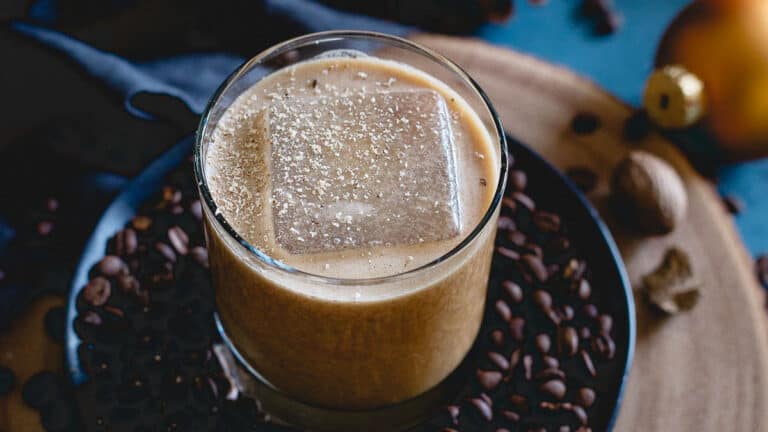 A glass of bourbon coffee nog with an ice cube in it.