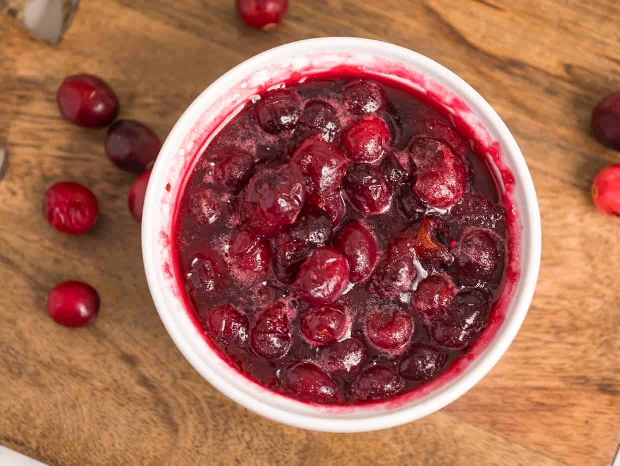 A bowl of cranberry sauce on a wooden cutting board.