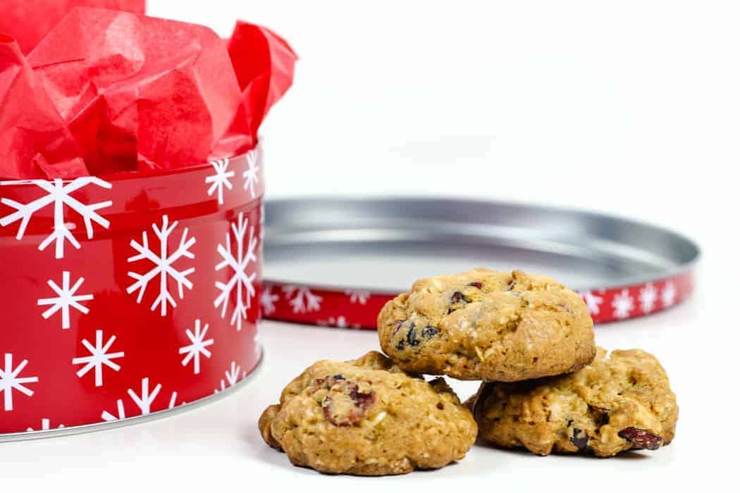 A stack of cranberry cookies next to a red cookie tin with snowfakes.