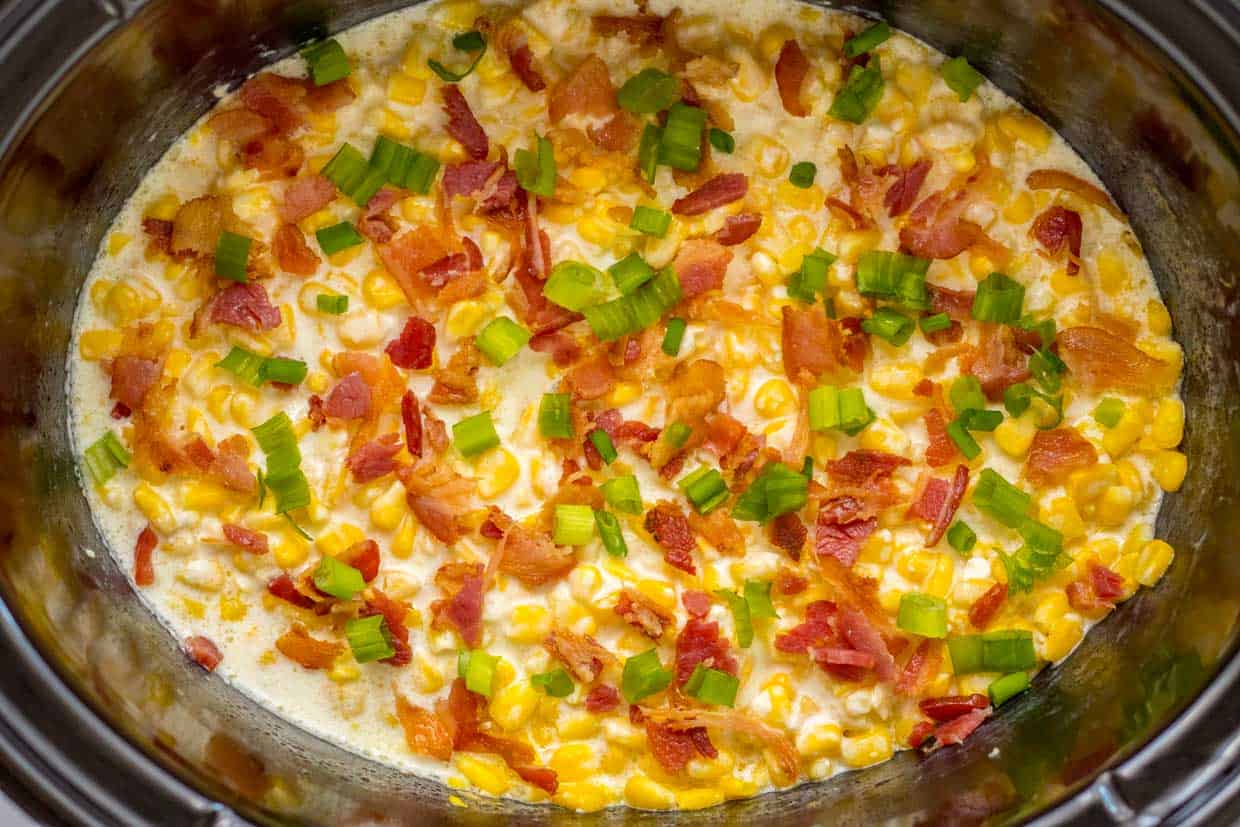 A crock pot filled with corn and bacon.