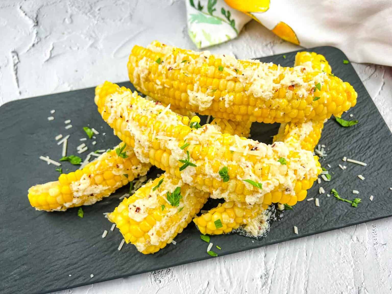 Corn on the cob with garlic parmesan on a black plate.