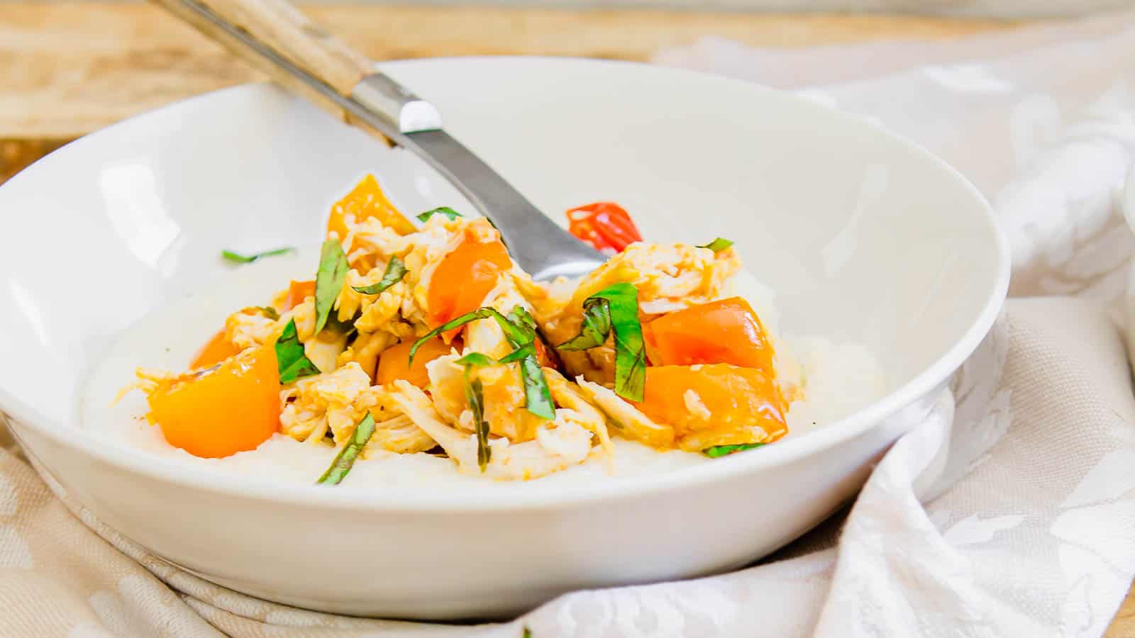 Creamy goat cheese grits in a white bowl with a wooden spoon topped with tomatoes and fresh basil.