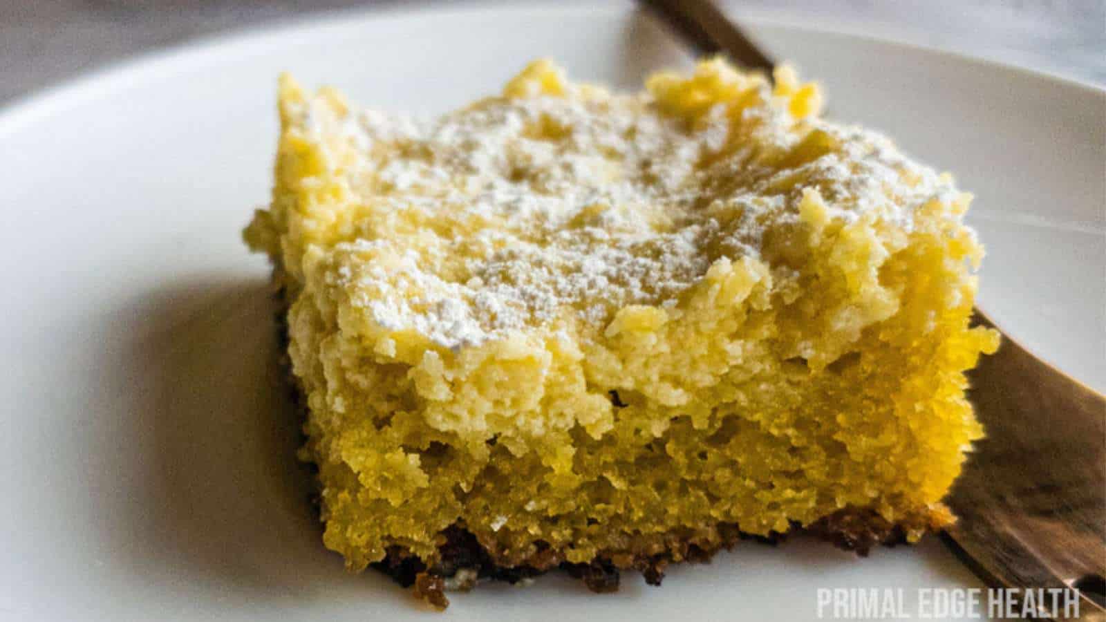 Square slice of ooey gooey butter cake on white plate with fork on the side.