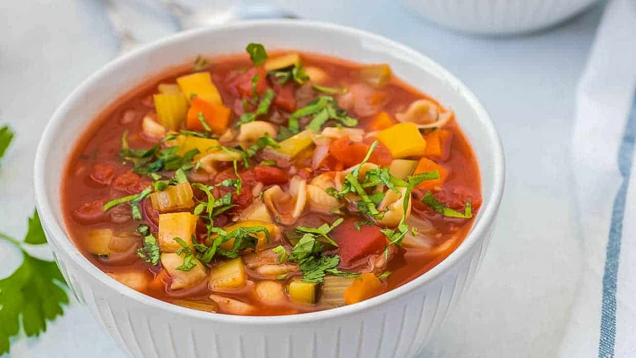 Olive Garden Minestrone Soup in a white bowl topped with basil.