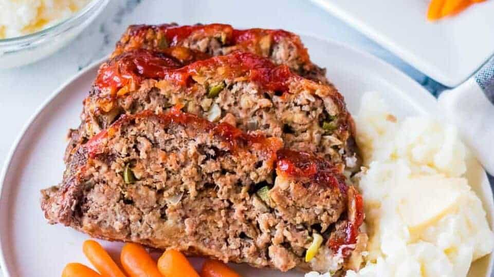 Two slices of meatloaf on a plate with mashed potatoes and carrots.