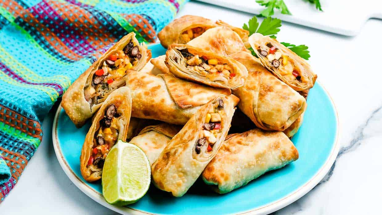 Plate of southwest egg rolls cut open to show the filling of beans, chicken, corn and cheese.