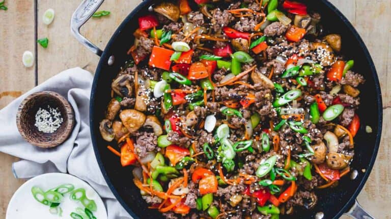 A skillet full of vegetables and meat on a wooden table.