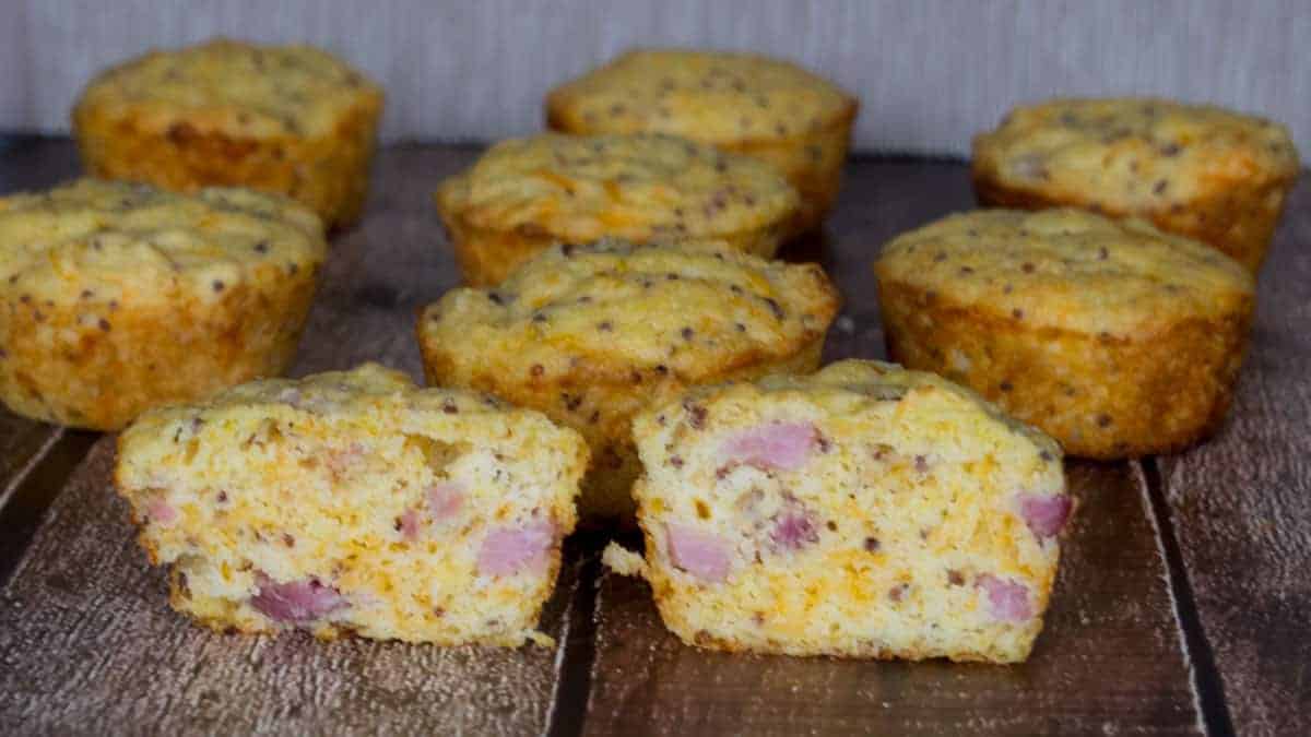 Ham and cheese muffins on a wooden table with one cut in half.