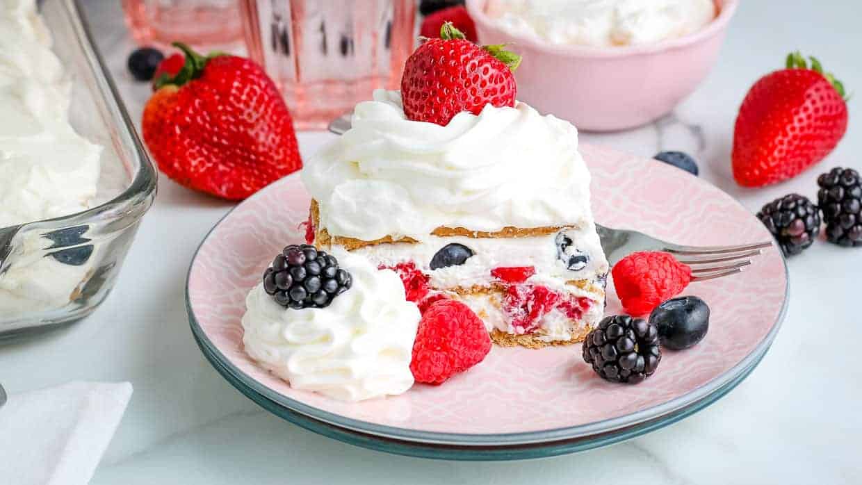 Icebox cake with raspberries, blueberries and strawberries on a pink plate.