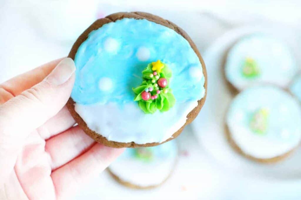 A person holding a cookie decorated with icing and a snowflake.