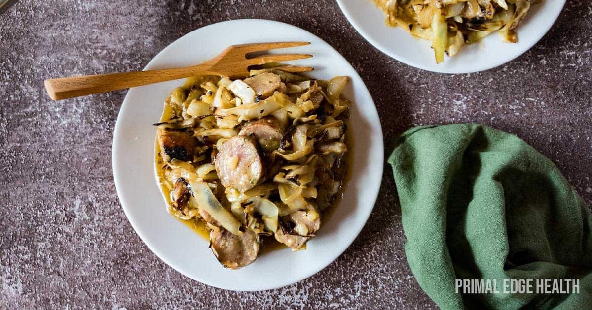 A picture of cabbage sausage white plate wooden fork.