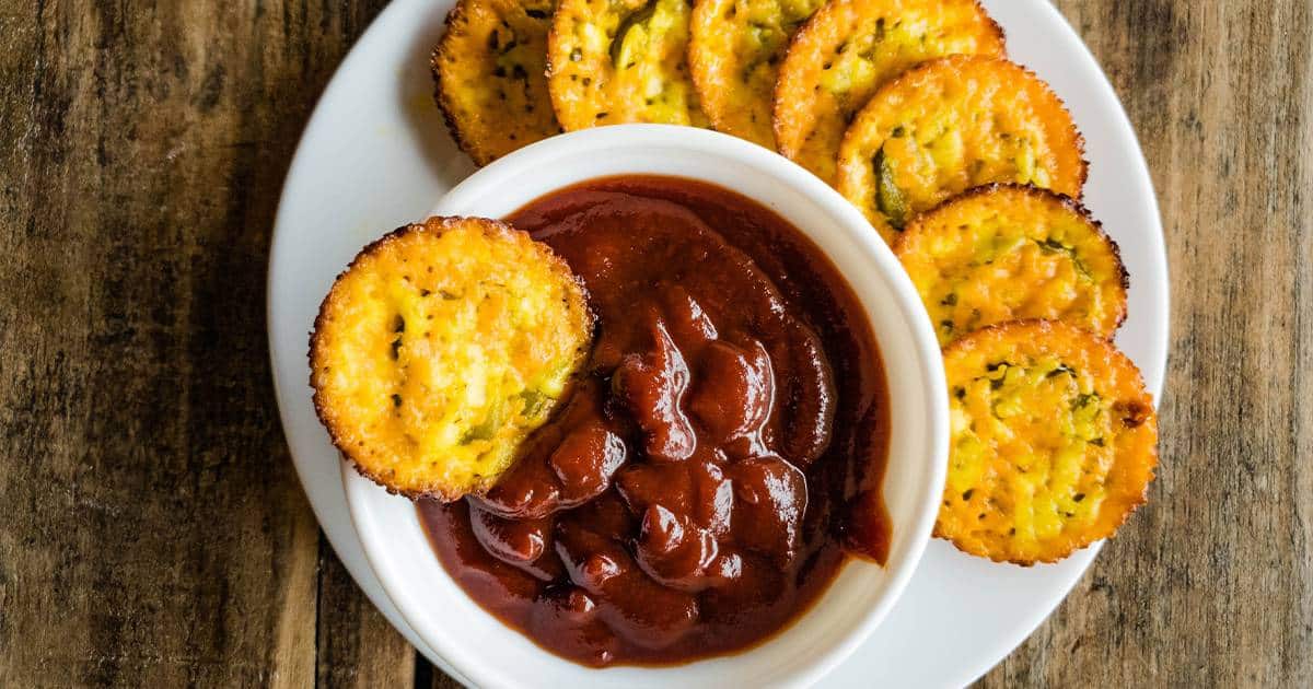 Baked pickle cheese chips with bowl of ketchup on white plate.