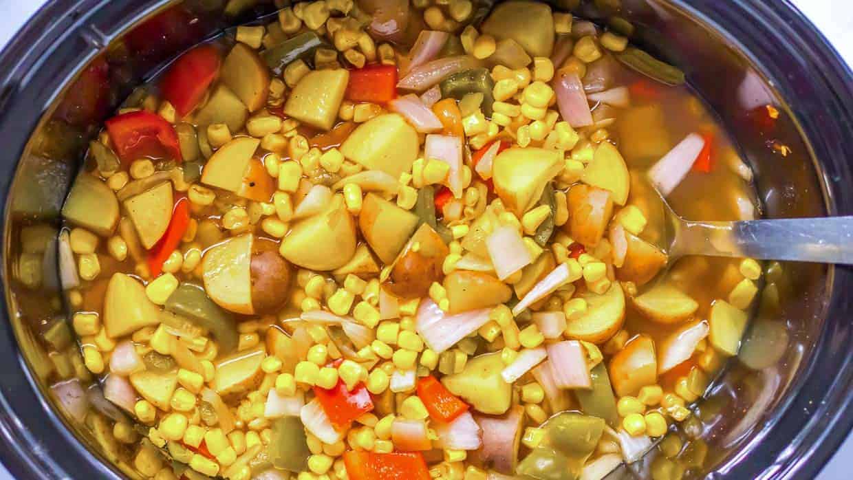 Street corn soup with potatoes, corn and red pepper in the crock pot with a spoon on the side.