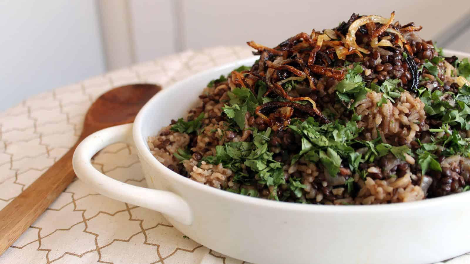 A bowl of brown rice and greens with a wooden spoon.