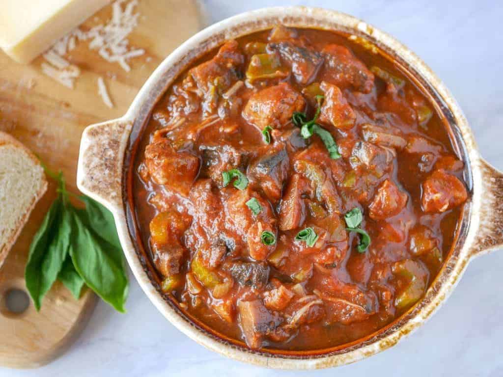 A bowl of mushroom stew with bread on a cutting board.