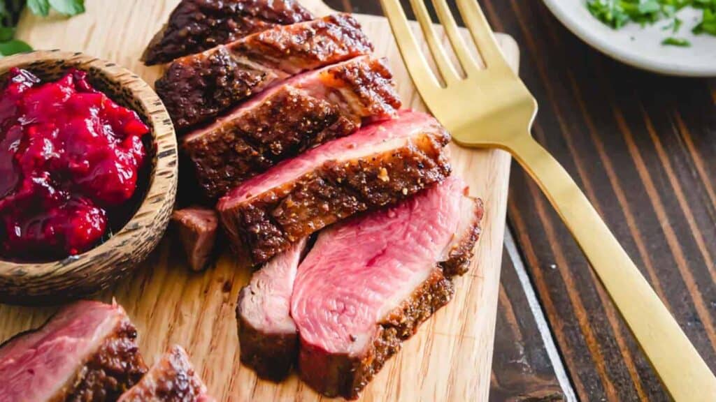 Sliced duck with cranberry sauce on a wooden cutting board.