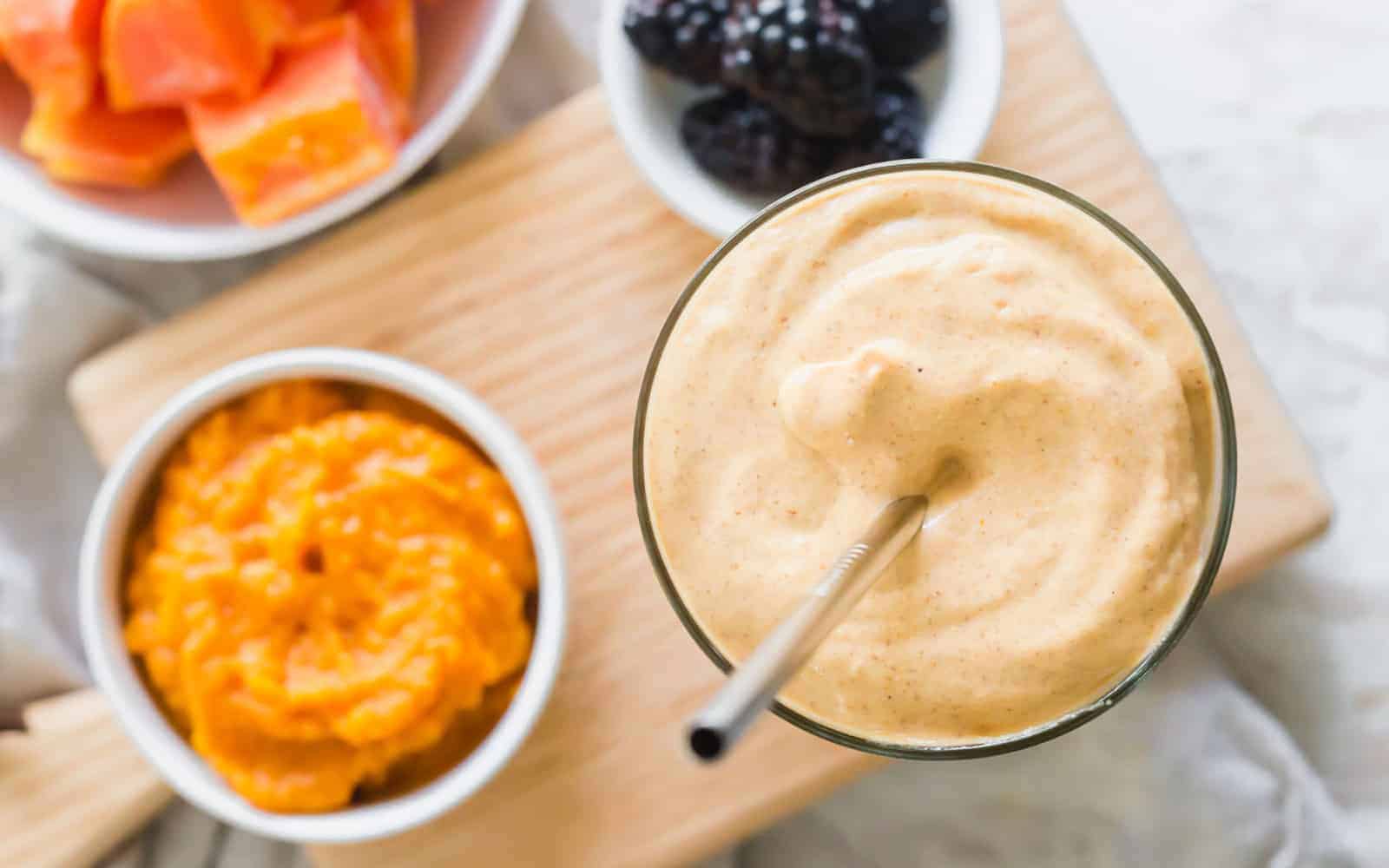 Papaya pumpkin gut healing smoothie in a glass with metal straw.