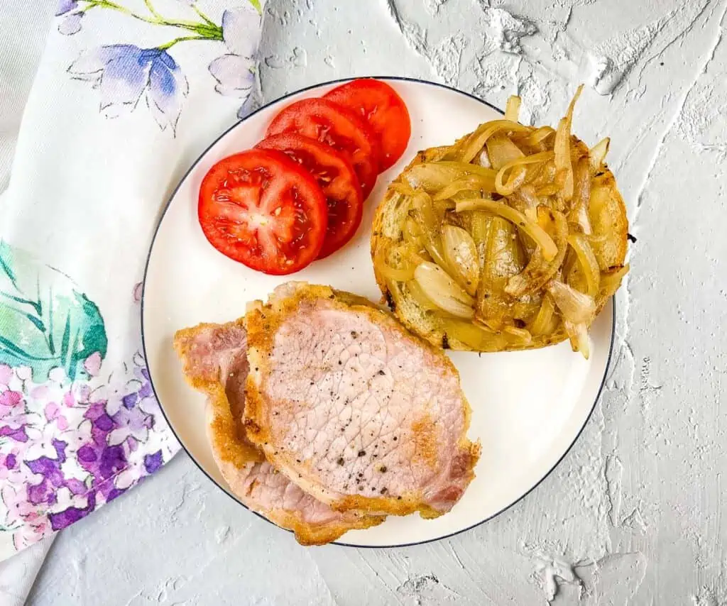 Peameal bacon on a plate with tomatoes and onions.