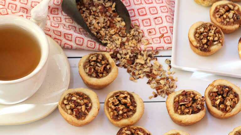 A cup of tea next to a plate of cookies with pecans.